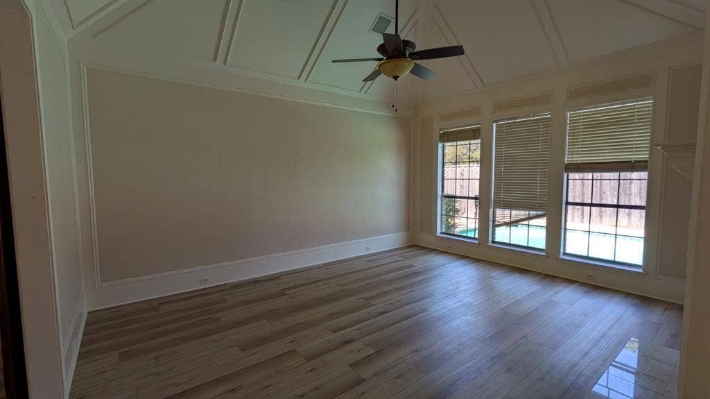 Wood-finish flooring, coffered ceiling, ceiling fan, and multiple large windows with horizontal blinds