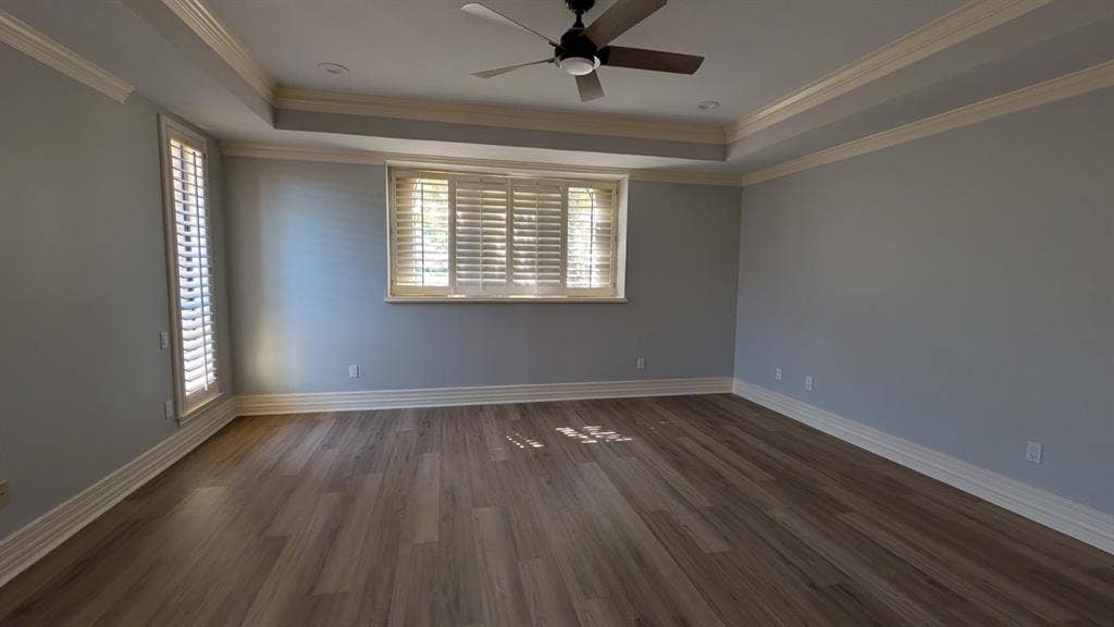 Expansive room featuring wood-finish flooring, a tray ceiling with recessed lighting, and a ceiling fan