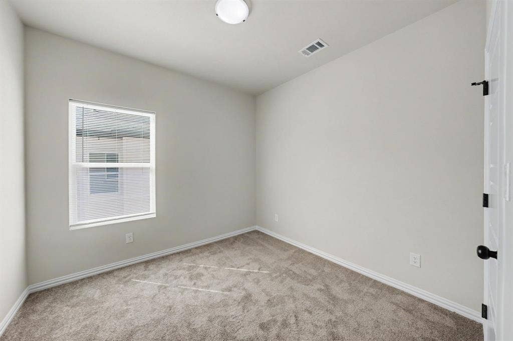 Carpeted flooring, single window with blinds, white trim, flush mount ceiling light, and a white paneled door with dark hardware
