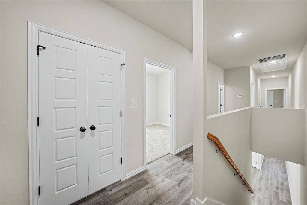 Hallway featuring wood-finish flooring, recessed lighting, and a wood handrail