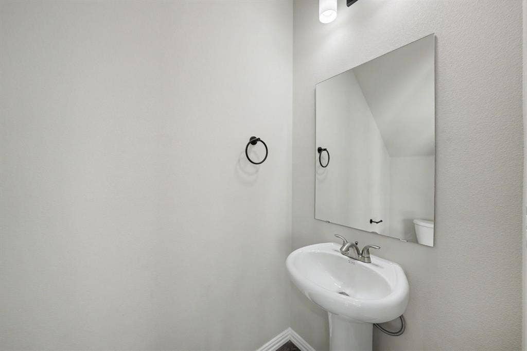 Pedestal sink with a chrome faucet, large wall-mounted mirror, and overhead vanity lighting