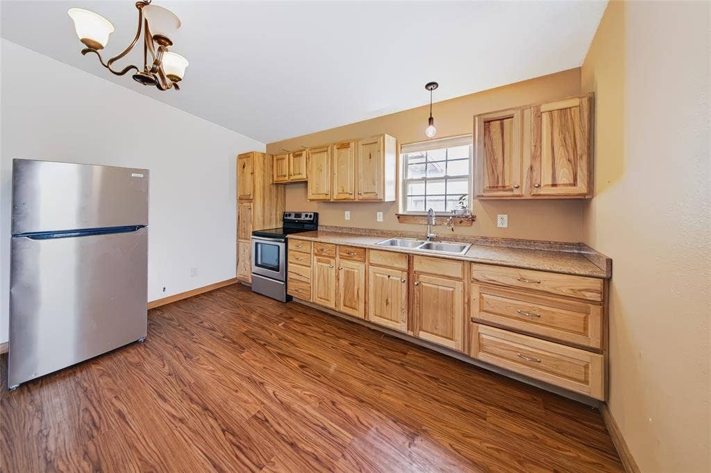 560 Green Acres Road, Weatherford, TX 76088 Wood-finish flooring, natural wood cabinetry, stainless steel appliances, double basin sink, and a multi-light chandelier