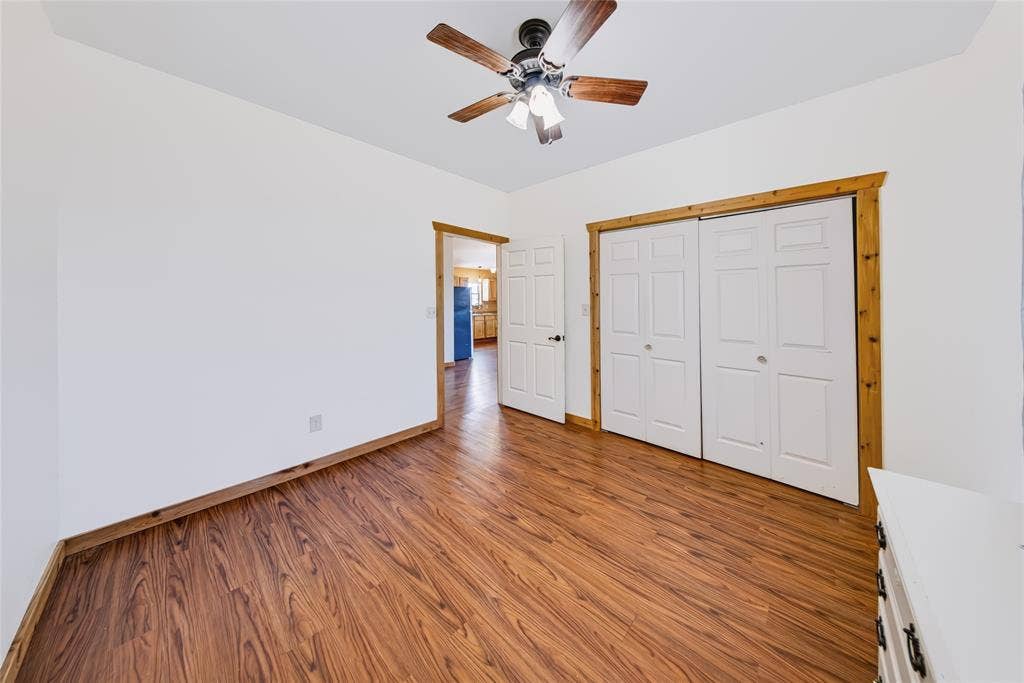 560 Green Acres Road, Weatherford, TX 76088 Wood-finish flooring, white walls, wood trim, white bi-fold closet doors, and a ceiling fan with integrated lighting