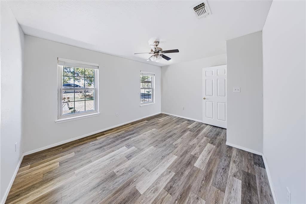560 Green Acres Road, Weatherford, TX 76088 Main home — second bedroom. Wood-finish flooring, two large windows, overhead ceiling fan, and a paneled door