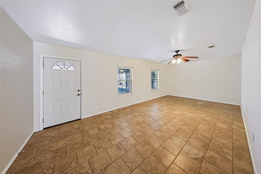 560 Green Acres Road, Weatherford, TX 76088 Main Home – Expansive room featuring tile flooring, a ceiling fan with integrated lighting, two windows, and a white entry door with an arched window insert