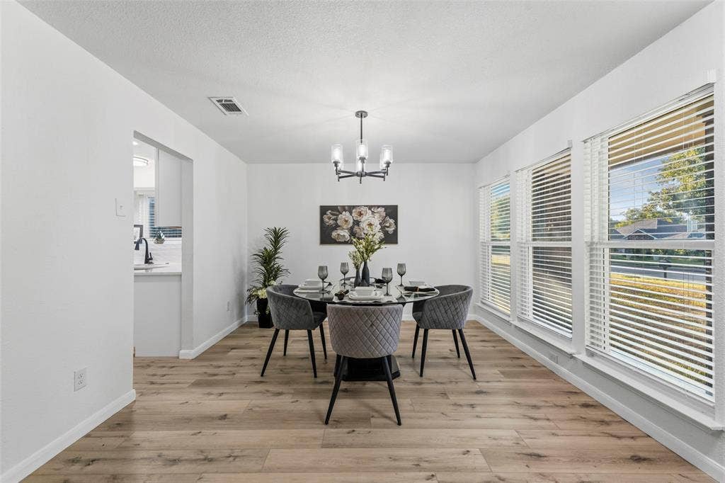 Bright dining area featuring multiple large windows, wood-finish flooring, and a contemporary chandelier