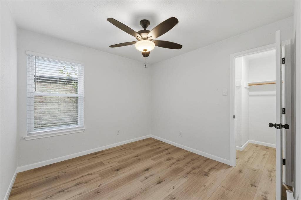 Wood-finish flooring, ceiling fan, window with blinds, and a built-in closet with shelving