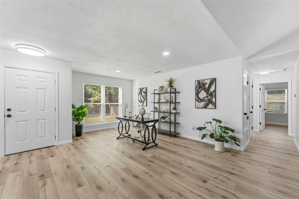 Recessed and flush-mount ceiling lighting illuminate an open-concept room with wood-finish flooring, white walls, and a multi-pane window