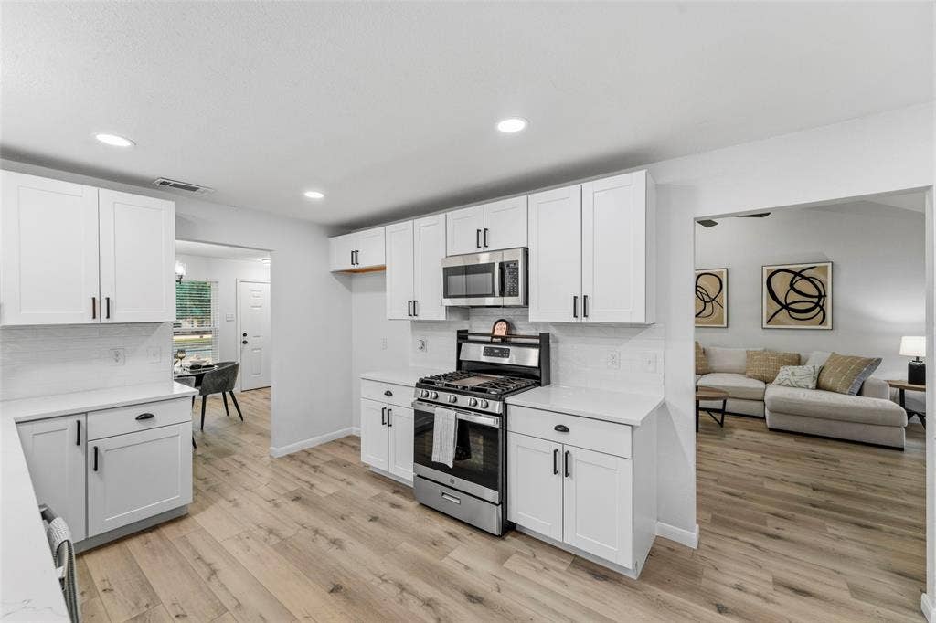 Modern kitchen featuring white shaker cabinets, white countertops, stainless steel appliances, wood-finish flooring, and recessed lighting