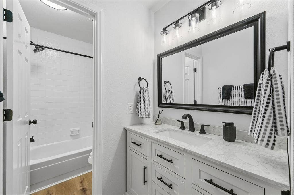 White vanity with integrated sink, black hardware, and a stone-finish countertop