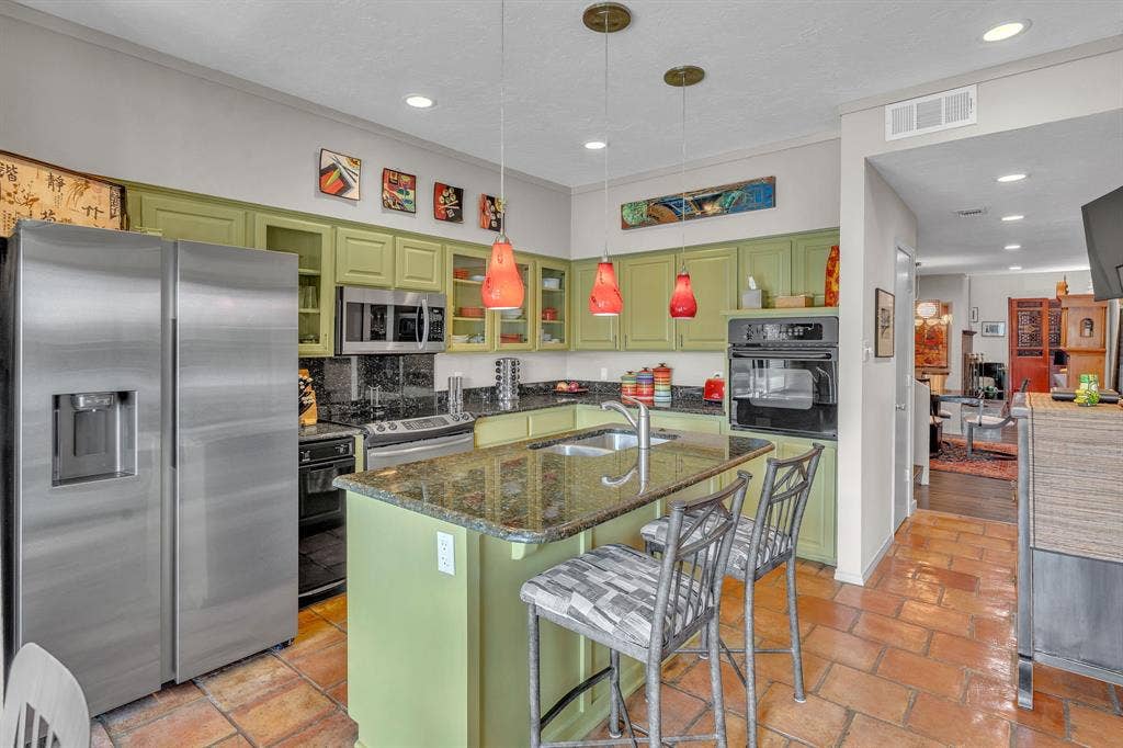 Kitchen with Saltillo tile flooring, cosmopolitan pendants, & bar seating.