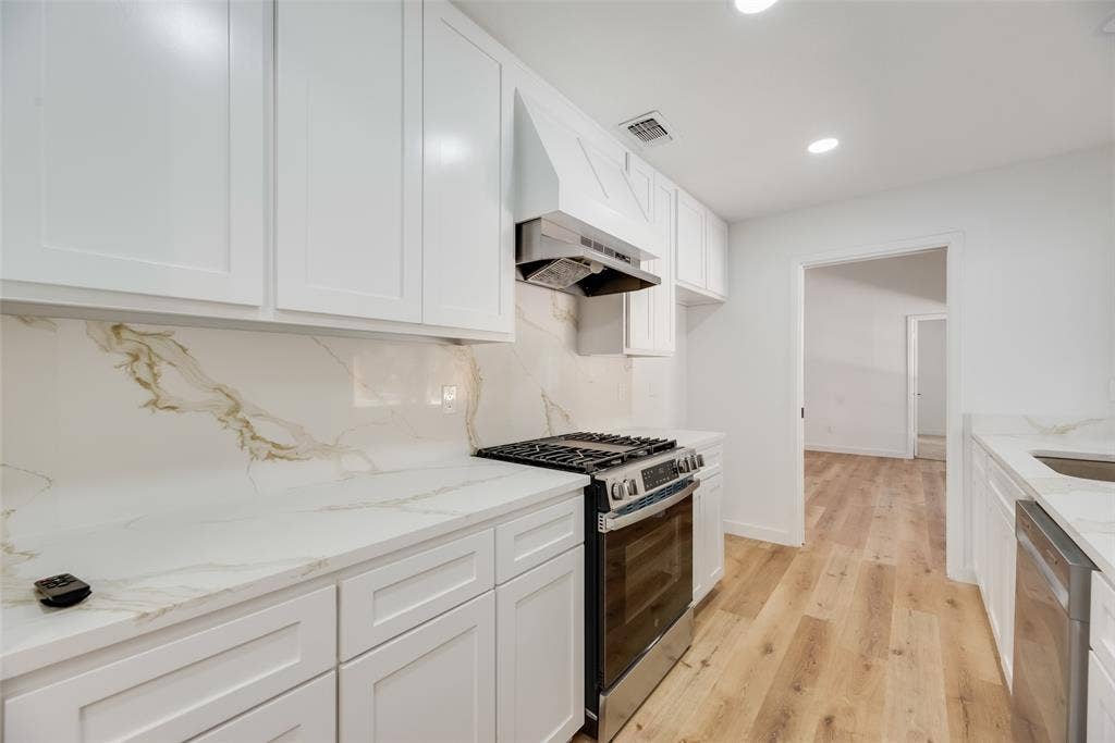 1903 Clemson Drive, Richardson, TX 75081 White shaker-style cabinetry, stainless steel range, white countertops with veining, matching backsplash, and light wood-finish flooring