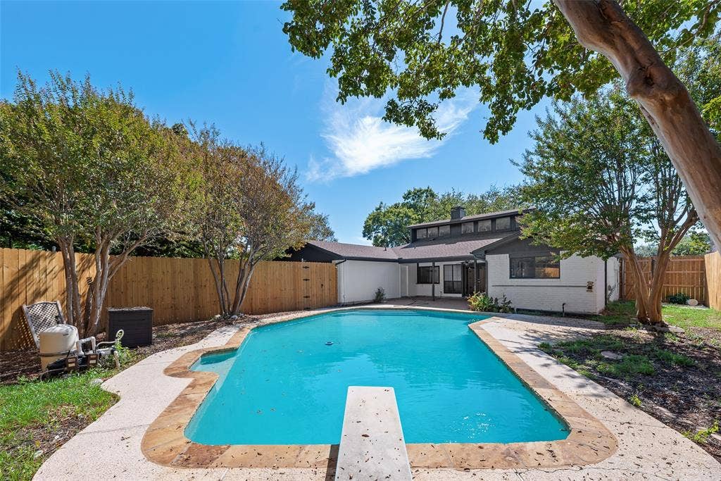 1903 Clemson Drive, Richardson, TX 75081 Private backyard with a rectangular swimming pool featuring a diving board, surrounding concrete patio, and mature trees