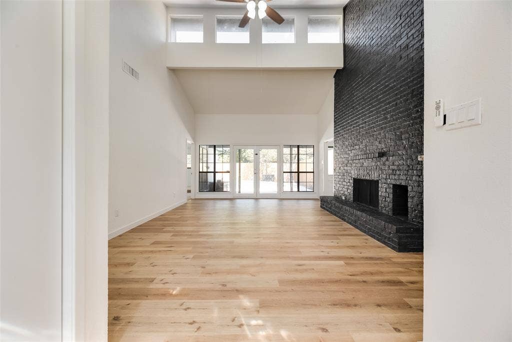 1903 Clemson Drive, Richardson, TX 75081 Vaulted ceiling with a ceiling fan, brick fireplace with a raised hearth, wood-finish flooring, and large windows with transom windows above