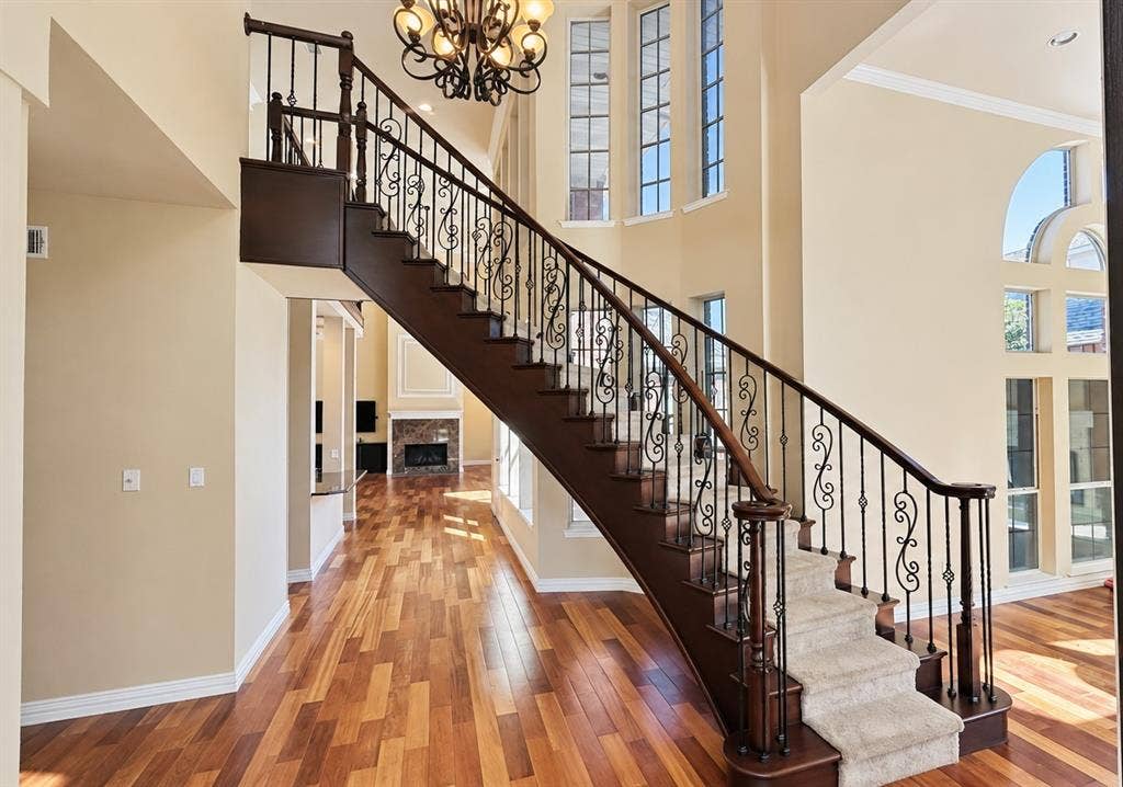 4505 Southgate Drive, Plano, TX 75024 Hardwood flooring, grand staircase with wrought iron balusters and carpeted treads, chandelier lighting fixture, and high ceilings with multiple windows