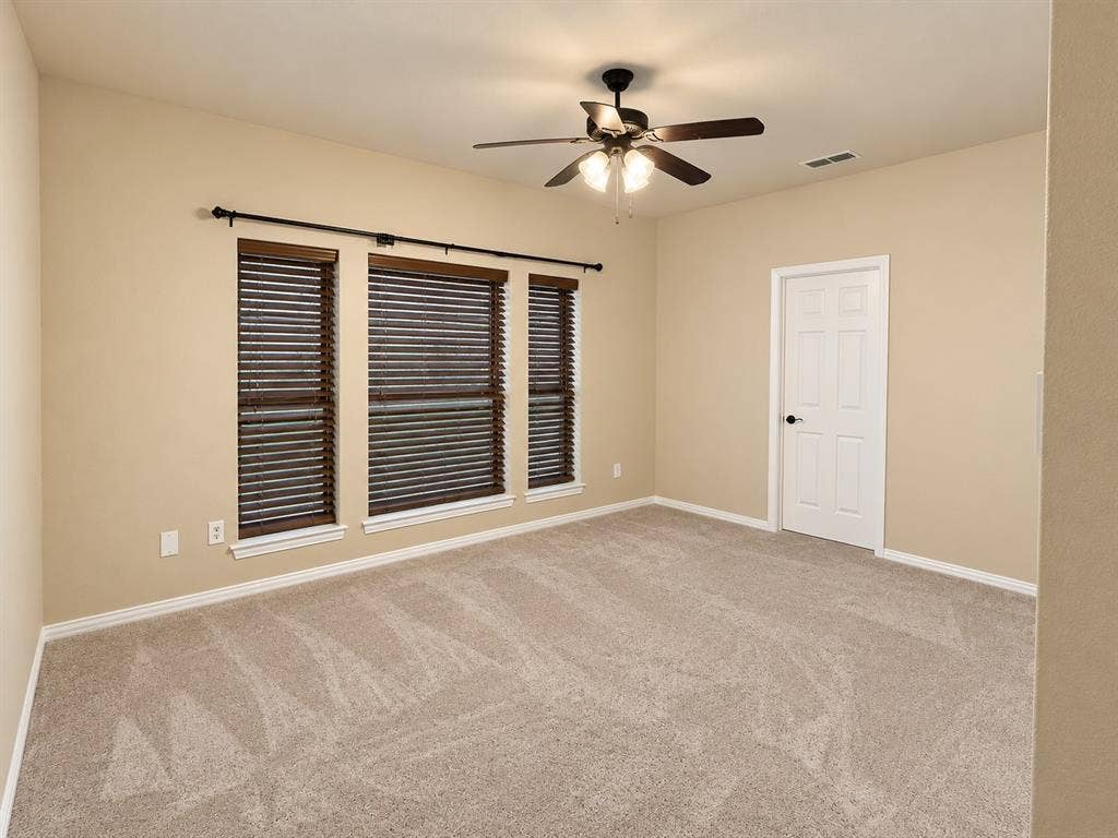 4505 Southgate Drive, Plano, TX 75024 Neutral-toned walls, light-colored carpet, ceiling fan with integrated lighting, three windows with wood-finish blinds, and a paneled door