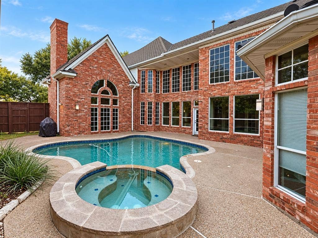 4505 Southgate Drive, Plano, TX 75024 Red brick exterior featuring an in-ground swimming pool, an integrated spa, extensive fenestration, and a stone-clad chimney