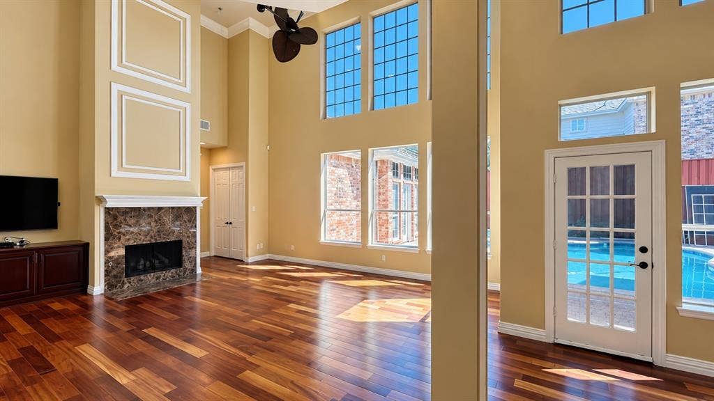 4505 Southgate Drive, Plano, TX 75024 Hardwood flooring throughout, tall ceilings, multiple large windows, a fireplace with a stone surround, and a glass-paned door
