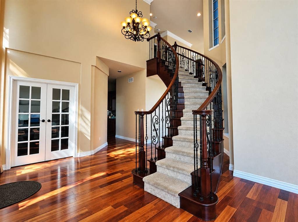 4505 Southgate Drive, Plano, TX 75024 Grand curved staircase with wrought iron balusters and wood-finish handrail, wood-finish flooring, double French doors with grid panes, and a decorative chandelier