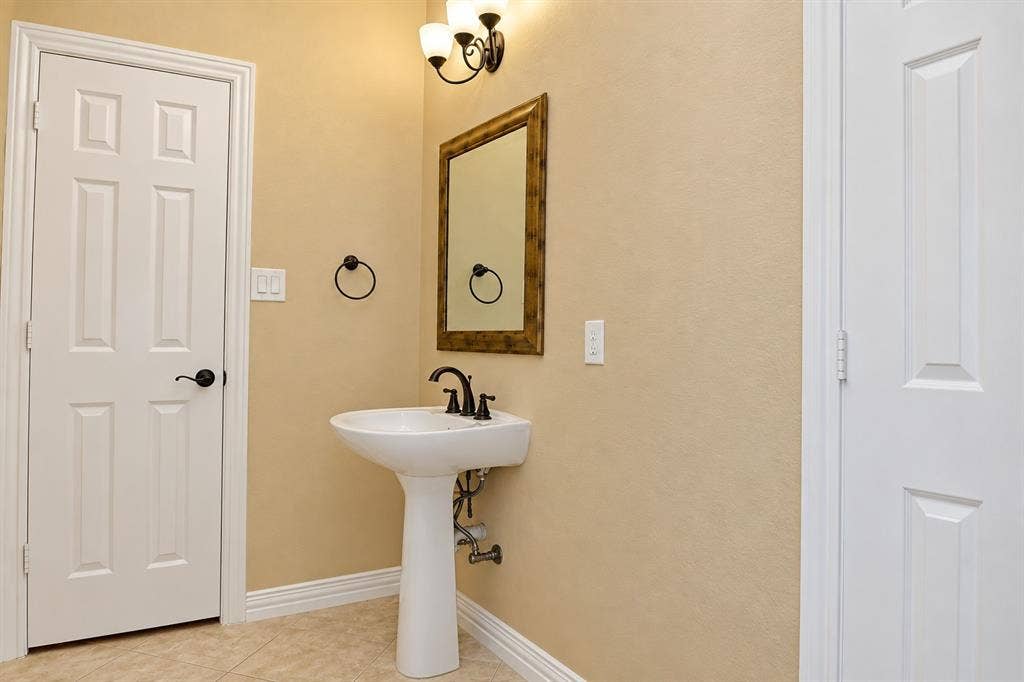 4505 Southgate Drive, Plano, TX 75024 Pedestal sink with dark bronze faucet, framed mirror, and wall-mounted light fixture