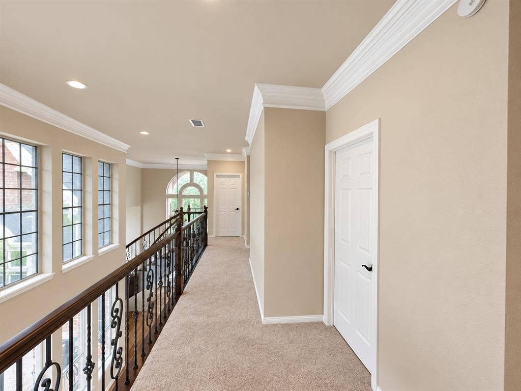 4505 Southgate Drive, Plano, TX 75024 Upper-level hallway featuring a decorative wrought iron railing, arched window, recessed lighting, and crown molding