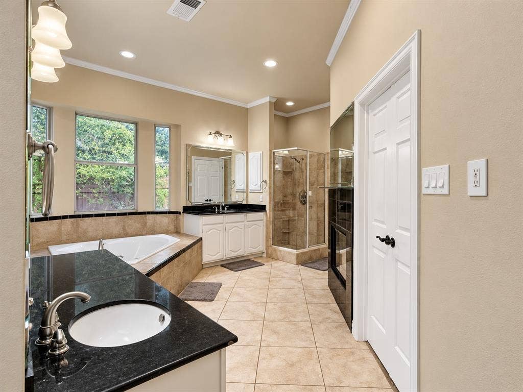 4505 Southgate Drive, Plano, TX 75024 Dual vanities with undermount sinks and dark countertops, separate soaking tub, and a glass-enclosed shower