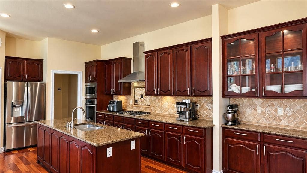 4505 Southgate Drive, Plano, TX 75024 Kitchen featuring wood-finish flooring, an island with an integrated sink, granite countertops, and stainless steel appliances