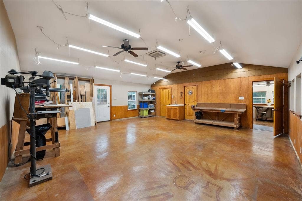 6472 Mark Drive, Burleson, TX 76028 Spacious room featuring a vaulted ceiling with multiple ceiling fans and strip lighting, wood-paneled walls, and a stained concrete floor