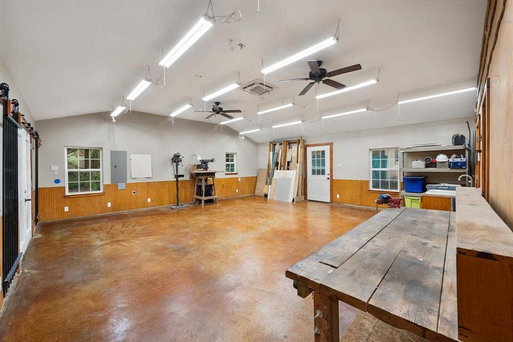 6472 Mark Drive, Burleson, TX 76028 Vaulted ceiling with multiple linear fluorescent light fixtures, two ceiling fans, and concrete-finish flooring