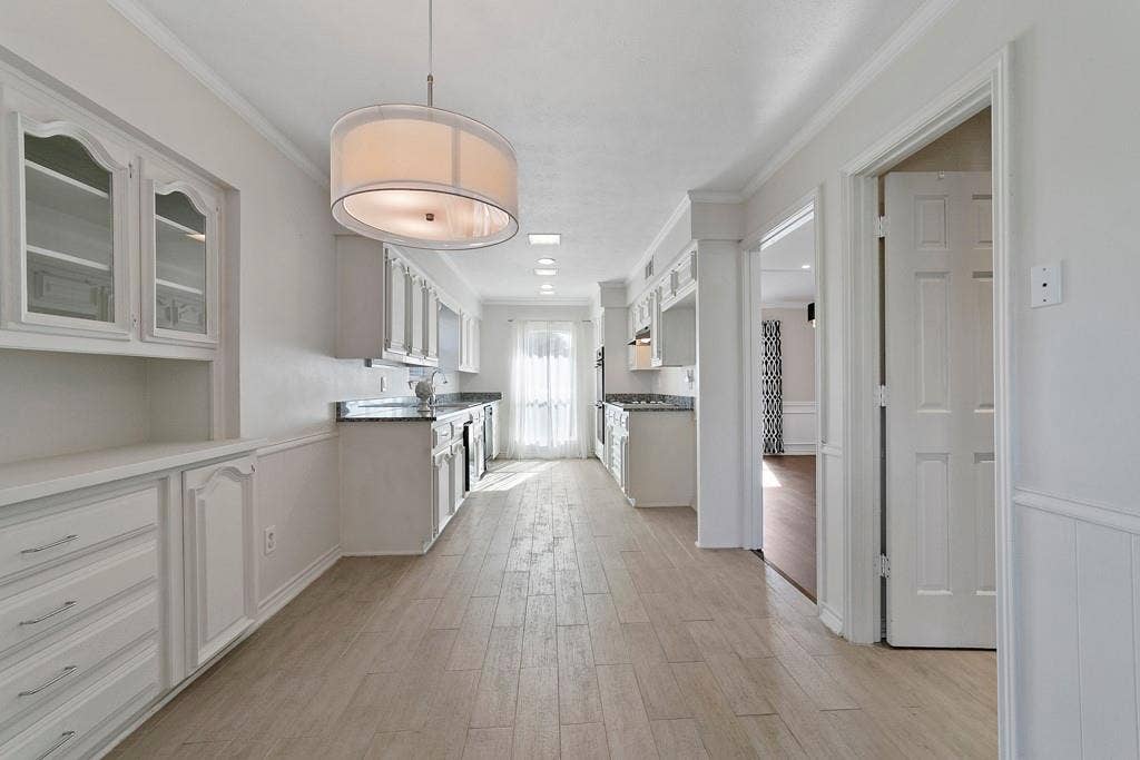 16353 Lauder Lane, Dallas, TX 75248 Galley kitchen featuring wood-finish flooring, white cabinetry, dark countertops, and a built-in buffet