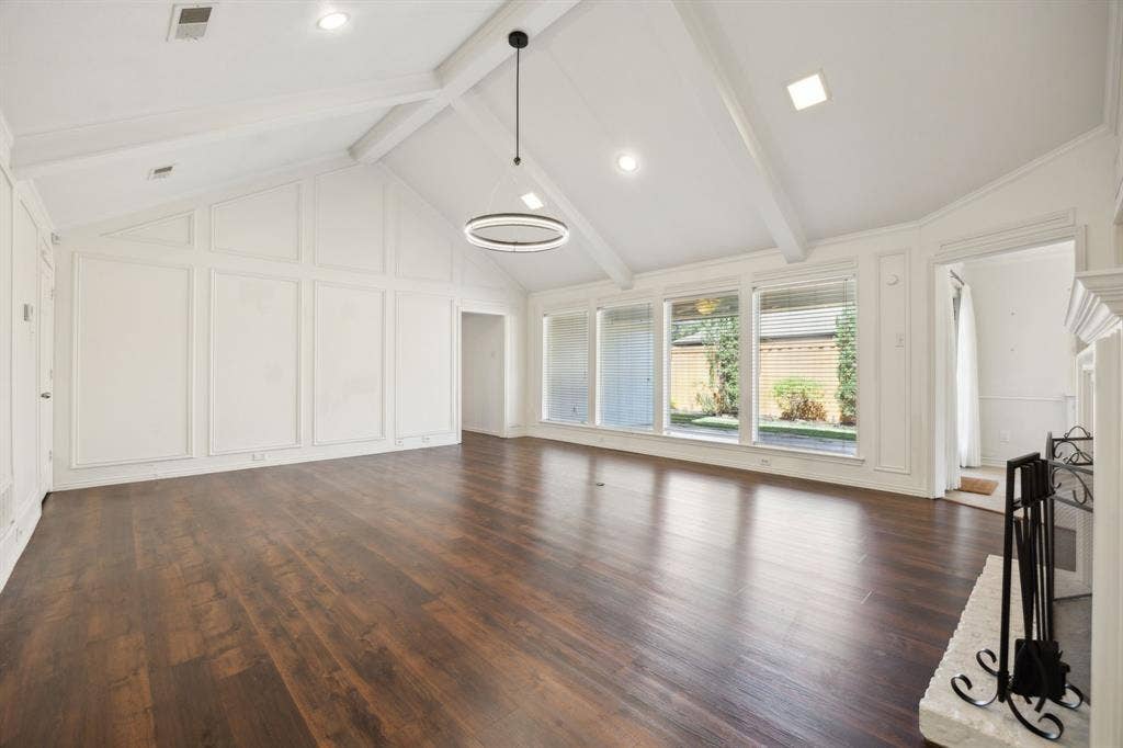 16353 Lauder Lane, Dallas, TX 75248 Vaulted ceiling with exposed beams, wood-finish flooring, accent wall paneling, modern circular chandelier, and a decorative fireplace surround