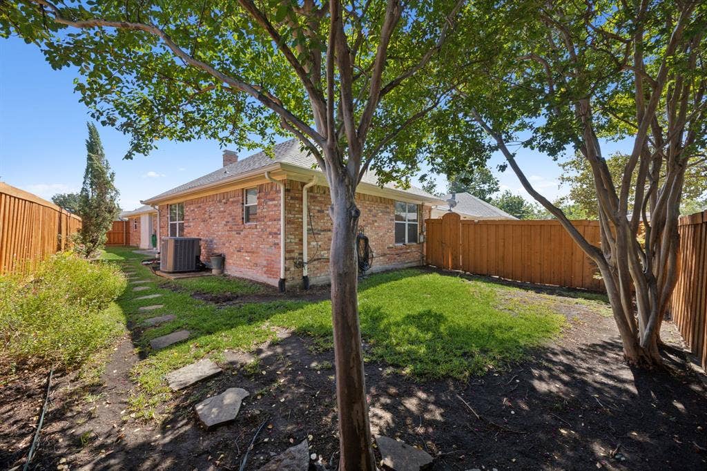 16353 Lauder Lane, Dallas, TX 75248 Private backyard with mature trees, a manicured lawn, and a stone-paver walkway, fully enclosed by a wood privacy fence