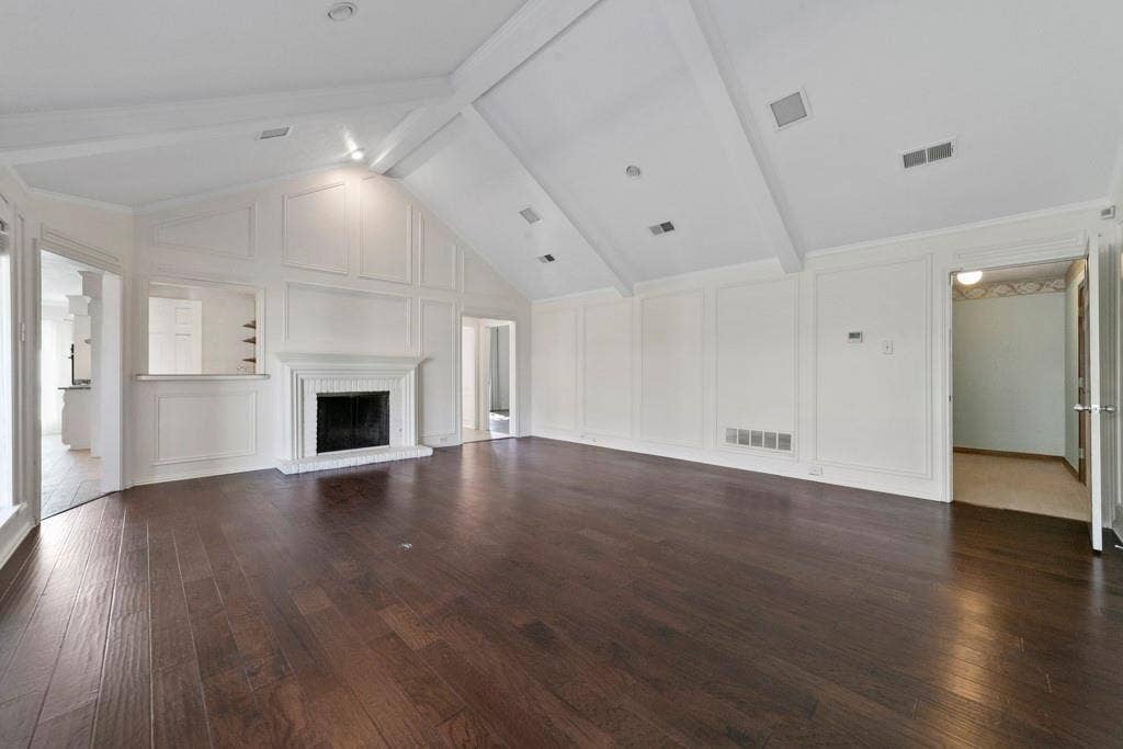 16353 Lauder Lane, Dallas, TX 75248 Vaulted ceilings with exposed beams, dark wood-finish flooring, white paneled walls, a fireplace with a mantel, and a pass-through window with a built-in shelf