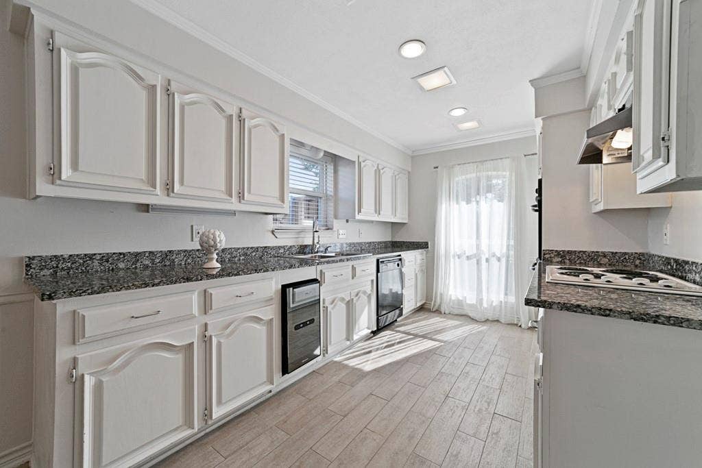 16353 Lauder Lane, Dallas, TX 75248 White cabinetry with decorative arch panels, speckled countertops, stainless steel sink, built-in cooktop with range hood, and wood-finish flooring