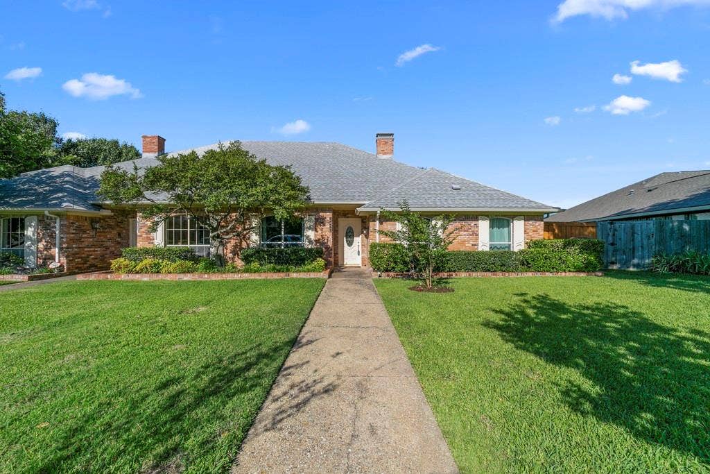 16353 Lauder Lane, Dallas, TX 75248 Brick exterior with a gray shingle roof, concrete walkway, and established landscaping