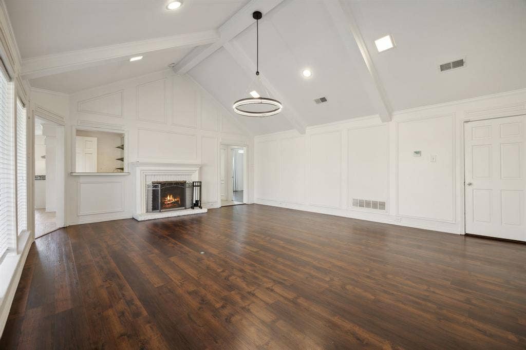 16353 Lauder Lane, Dallas, TX 75248 Spacious room with wood-finish flooring, a vaulted ceiling with exposed beams, and a fireplace featuring a white brick surround