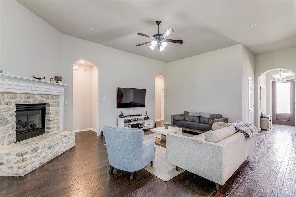 1481 Ramsbury Lane, Prosper, TX 75078 Spacious living area featuring high vaulted ceilings, stone fireplace, dark wood-finish flooring, and arched doorways