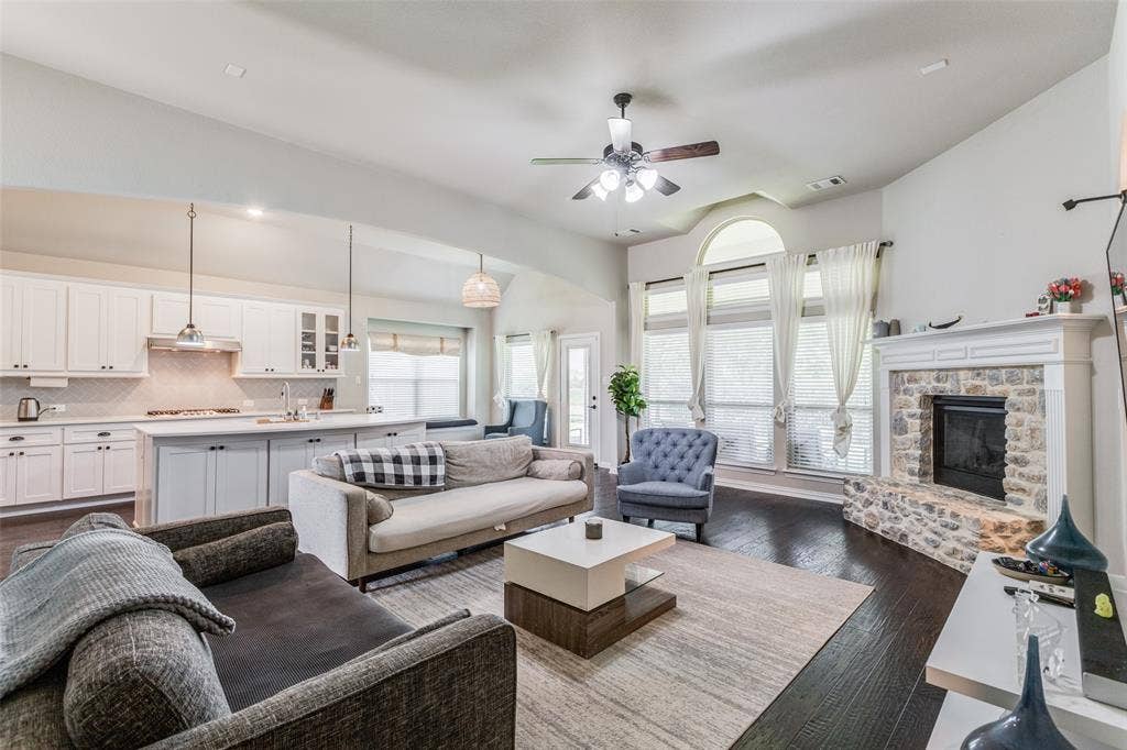 1481 Ramsbury Lane, Prosper, TX 75078 Wood-finish flooring, stone fireplace, vaulted ceiling with a fan, kitchen island with pendant lighting, and arched window