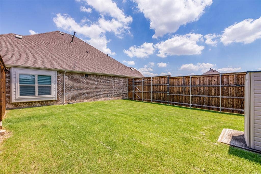1481 Ramsbury Lane, Prosper, TX 75078 Expansive grassy backyard featuring a full privacy fence, brick exterior, and a storage shed