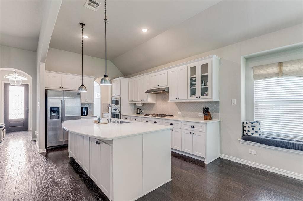 1481 Ramsbury Lane, Prosper, TX 75078 Kitchen featuring white cabinetry, a curved island with integrated sink, stainless steel appliances, and a window seat