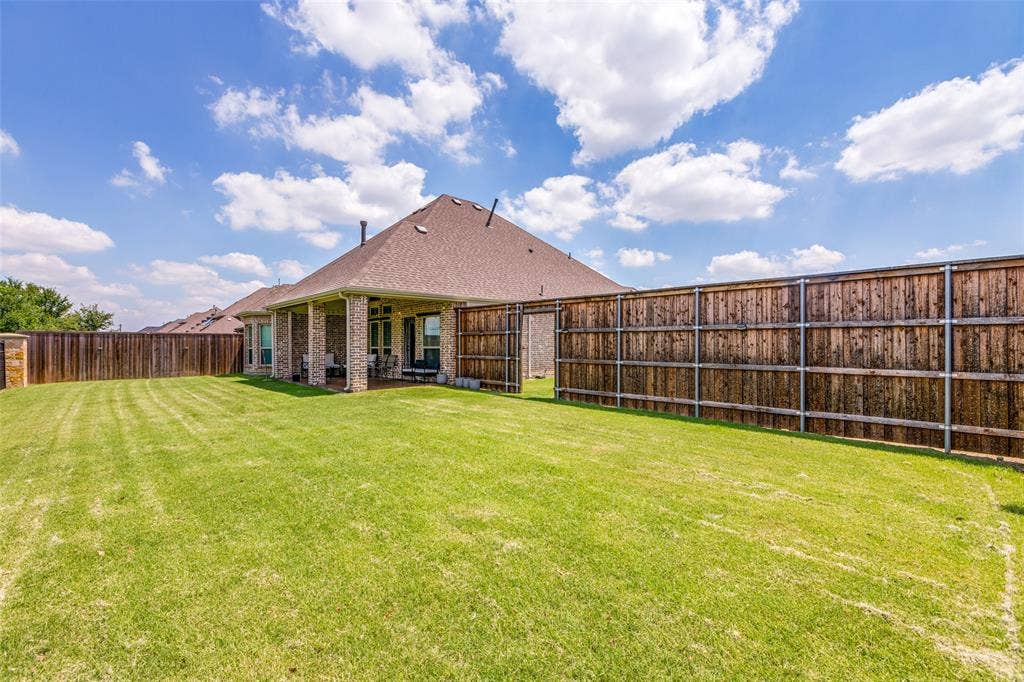 1481 Ramsbury Lane, Prosper, TX 75078 Expansive green lawn, wood privacy fencing, covered patio, brick exterior, and a shingle roof