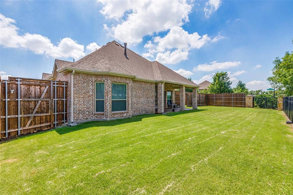 1481 Ramsbury Lane, Prosper, TX 75078 Brick exterior with multiple windows, covered patio with structural columns, expansive lawn, and wooden privacy fencing