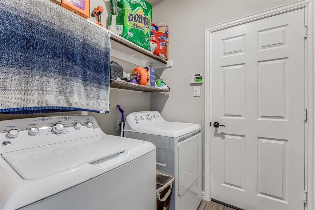 1481 Ramsbury Lane, Prosper, TX 75078 Laundry area featuring white appliances, floating wood-finish shelving, and a paneled door with dark hardware