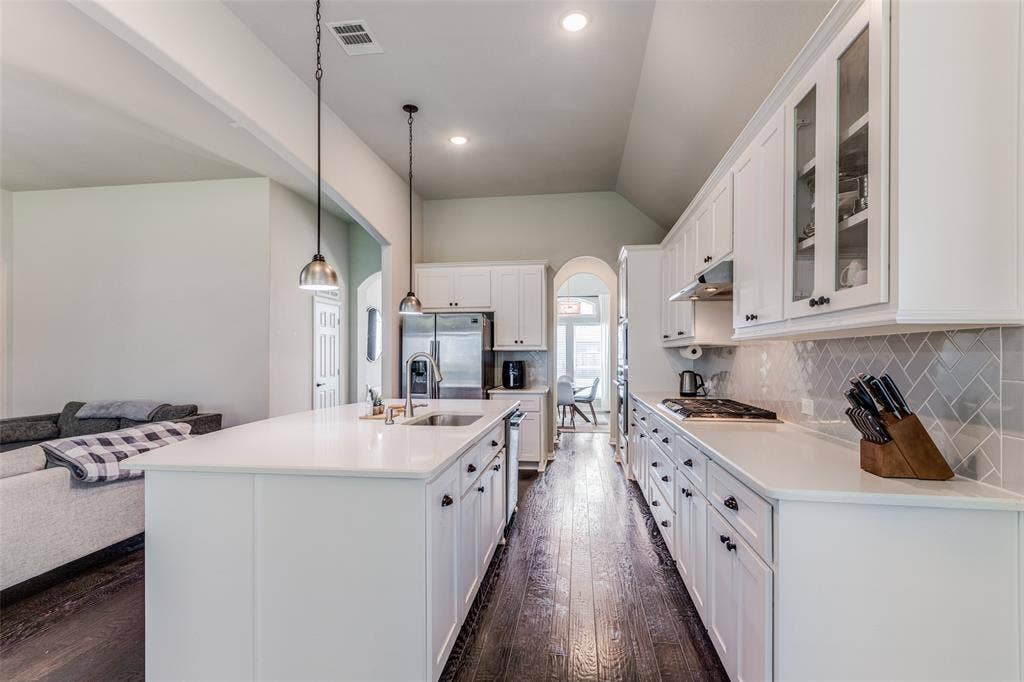 1481 Ramsbury Lane, Prosper, TX 75078 Kitchen featuring dark wood-finish flooring, white cabinetry, a large kitchen island with an undermount sink, and stainless steel appliances