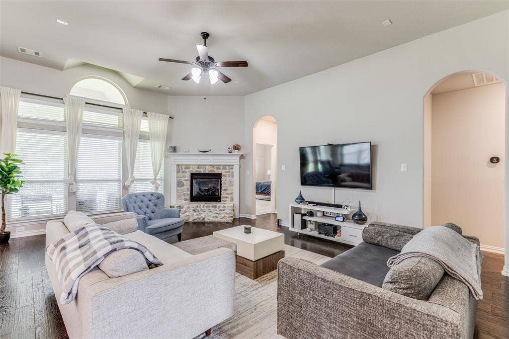1481 Ramsbury Lane, Prosper, TX 75078 Living area with wood-finish flooring, a stone-surround fireplace with a mantel, and an arched window