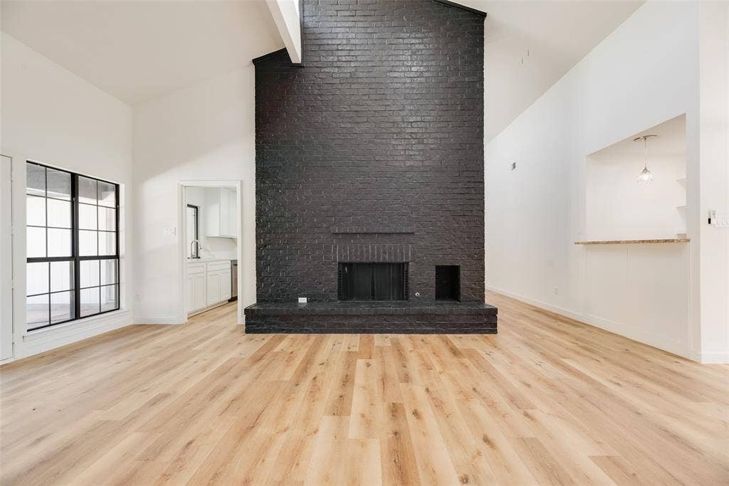 1903 Clemson Drive, Richardson, TX 75081 Vaulted ceilings, wood-finish flooring, a black painted brick fireplace, a pass-through window with a stone-finish countertop, and a large multi-pane window