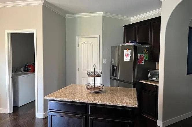 15009 Northview Drive, Little Elm, TX 75068 Kitchen island with a light-toned speckled countertop, dark wood-finish cabinetry, stainless steel refrigerator, and wood-finish flooring