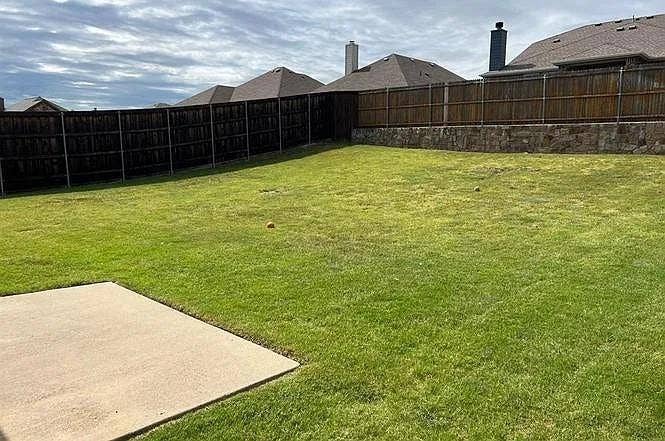 15009 Northview Drive, Little Elm, TX 75068 Expansive green lawn with a concrete patio, wood privacy fencing, and a stone retaining wall