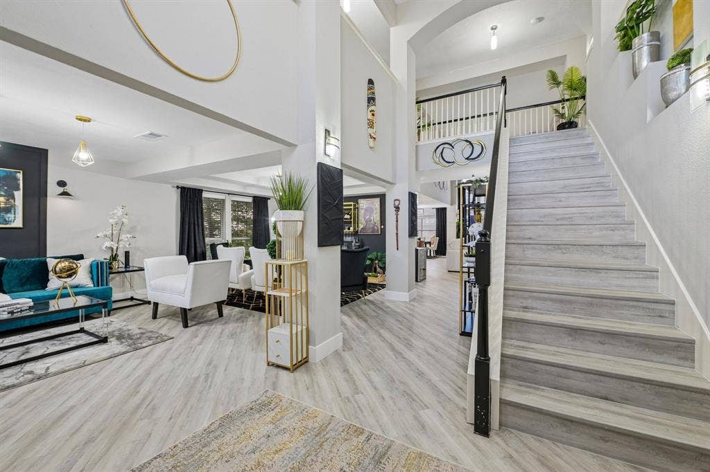 High ceilings, light wood-finish flooring, staircase with white spindles and black handrail, recessed lighting, and wall sconces