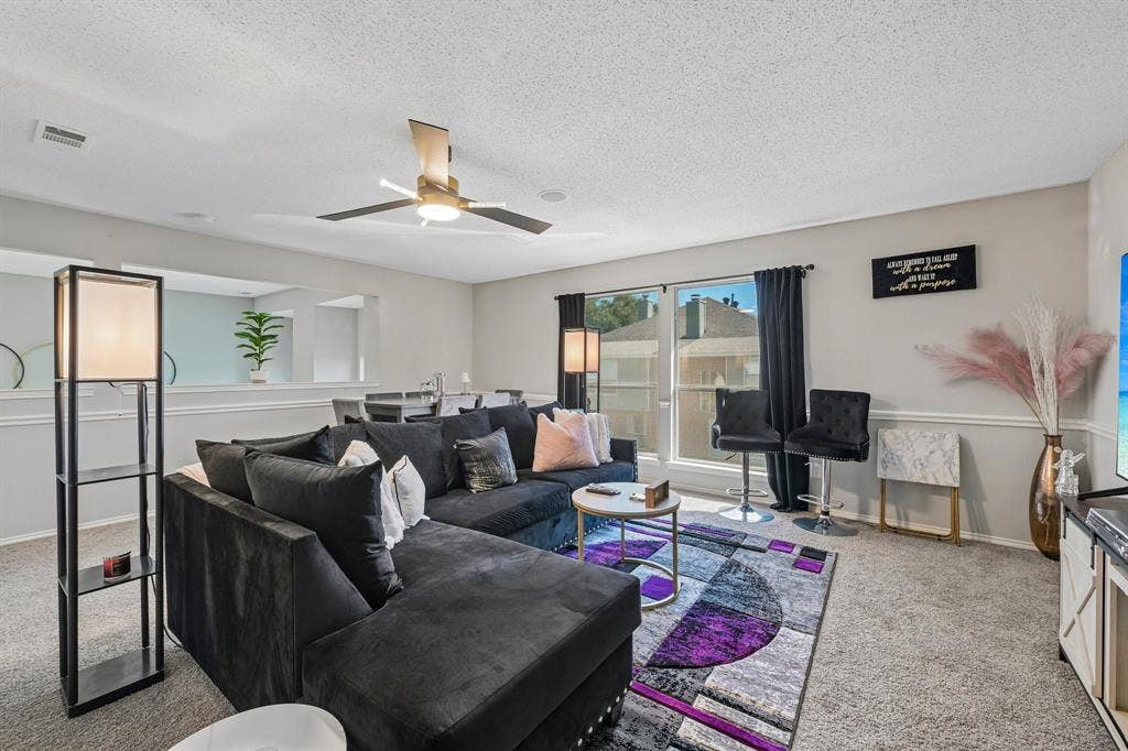 Recessed lighting, ceiling fan with integrated light, multiple windows with natural light, textured carpet flooring, and a half-wall partition